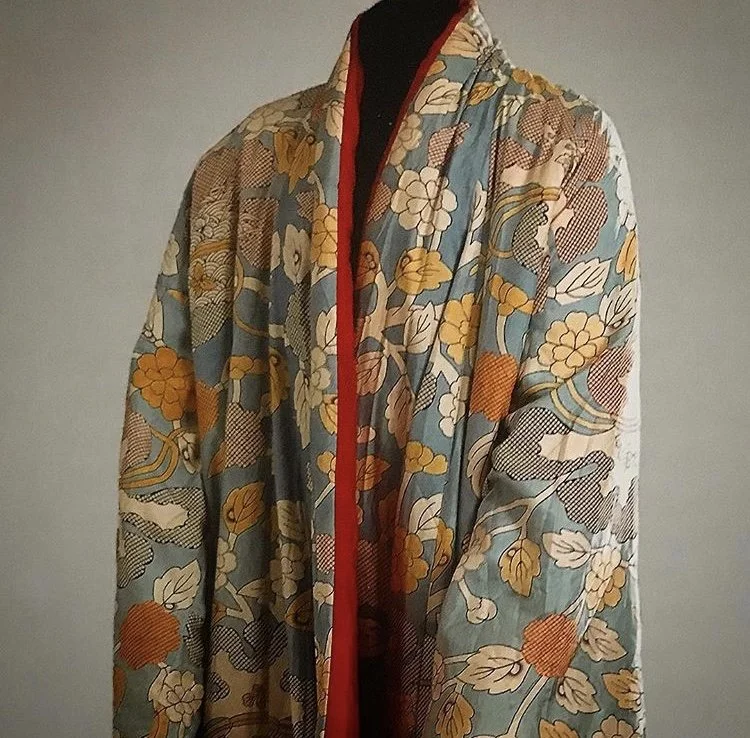 A floral-patterned quilt or textile with a mix of yellow, orange, white, and beige flowers and leaves, displayed on a black mannequin.