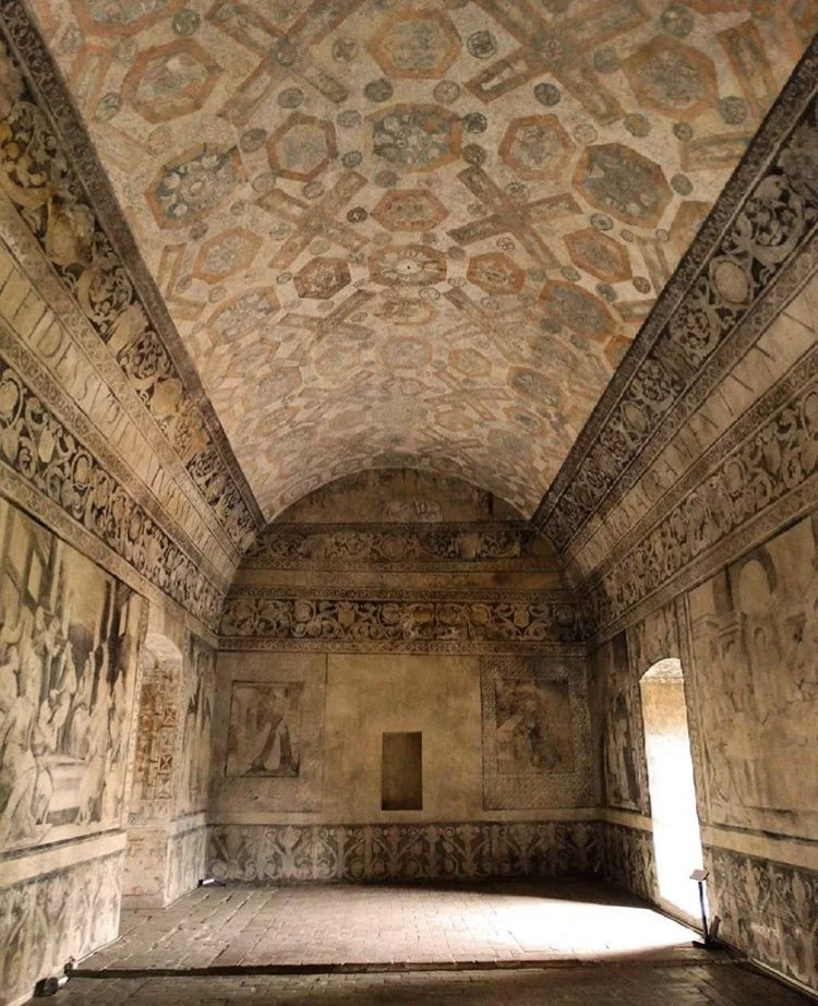 A historical room with intricate painted decorations on the ceiling and walls, featuring scenes and floral patterns, in an ancient European style.