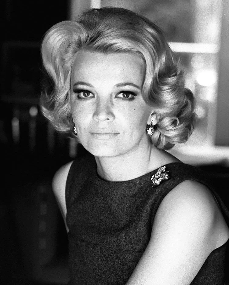 A woman with vintage-style curled hair wearing a sleeveless dress with rhinestone embellishments and earrings, looking directly at the camera in black and white.