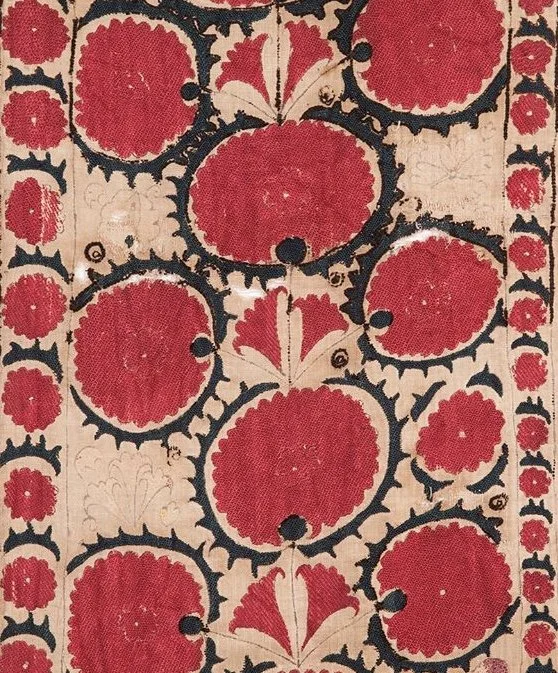 Close-up of a decorative textile or wall hanging with a pattern of red circular motifs outlined in black, interspersed with cream-colored background and floral elements.