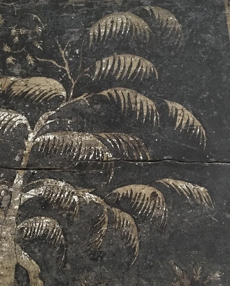 Close-up of a carved or painted decorative design of overlapping fern leaves in gold on a dark background.