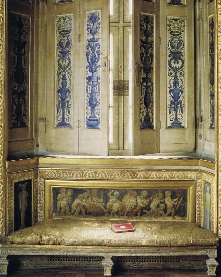 A vintage, gold-colored bench with intricate detailing and painted scenes, positioned beneath ornate, decorated wooden doors with blue and gold patterns.