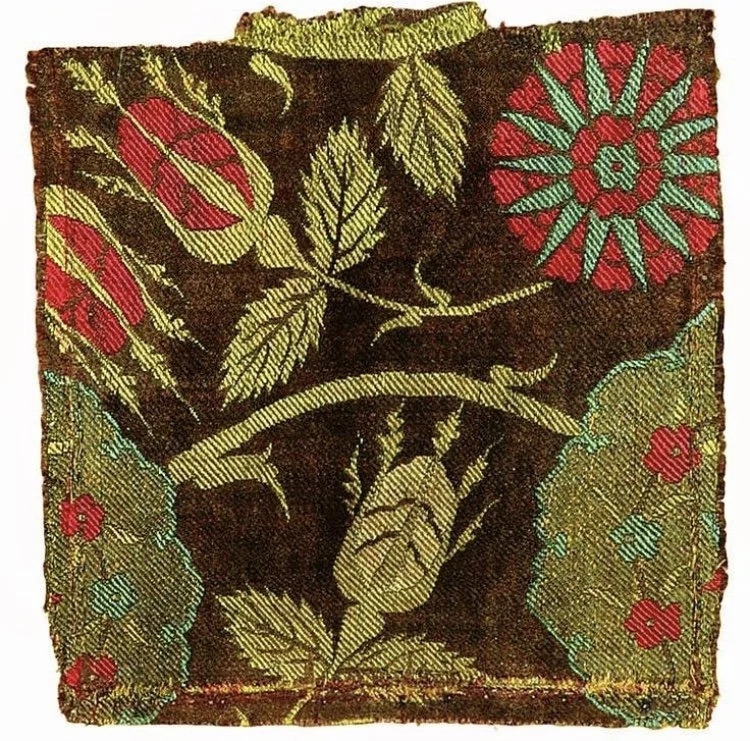Colorful embroidered textile featuring floral and leaf patterns in red, green, and gold on a dark background.