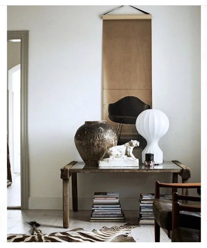 Decorative interior with a wooden console table, large ceramic vase, sculpture of a dog, modern white lamp, black chair, and stacks of books, with a zebra print rug on the floor.