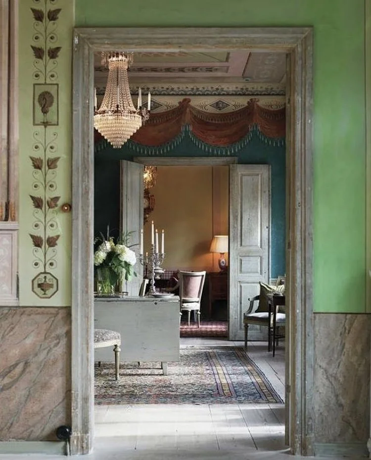 View through doorways into multiple rooms decorated in elegant, vintage style with chandeliers, floral arrangements, and antique furniture.