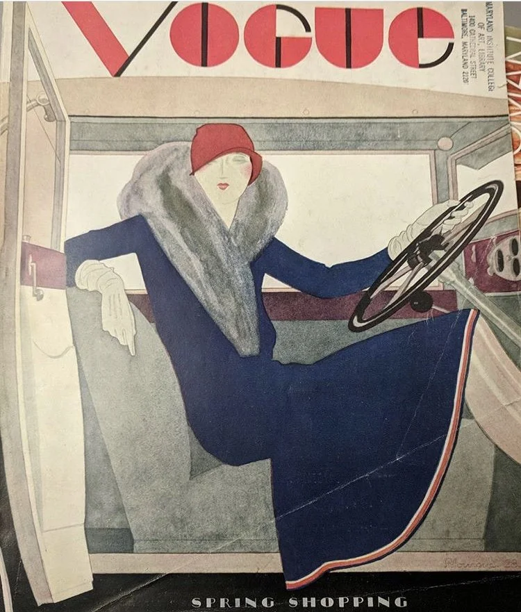 Vintage Vogue magazine cover featuring a stylized illustration of a woman sitting in a car, dressed in a long dark dress, red hat, and gray scarf, with the headline 'Spring Shopping' at the bottom.