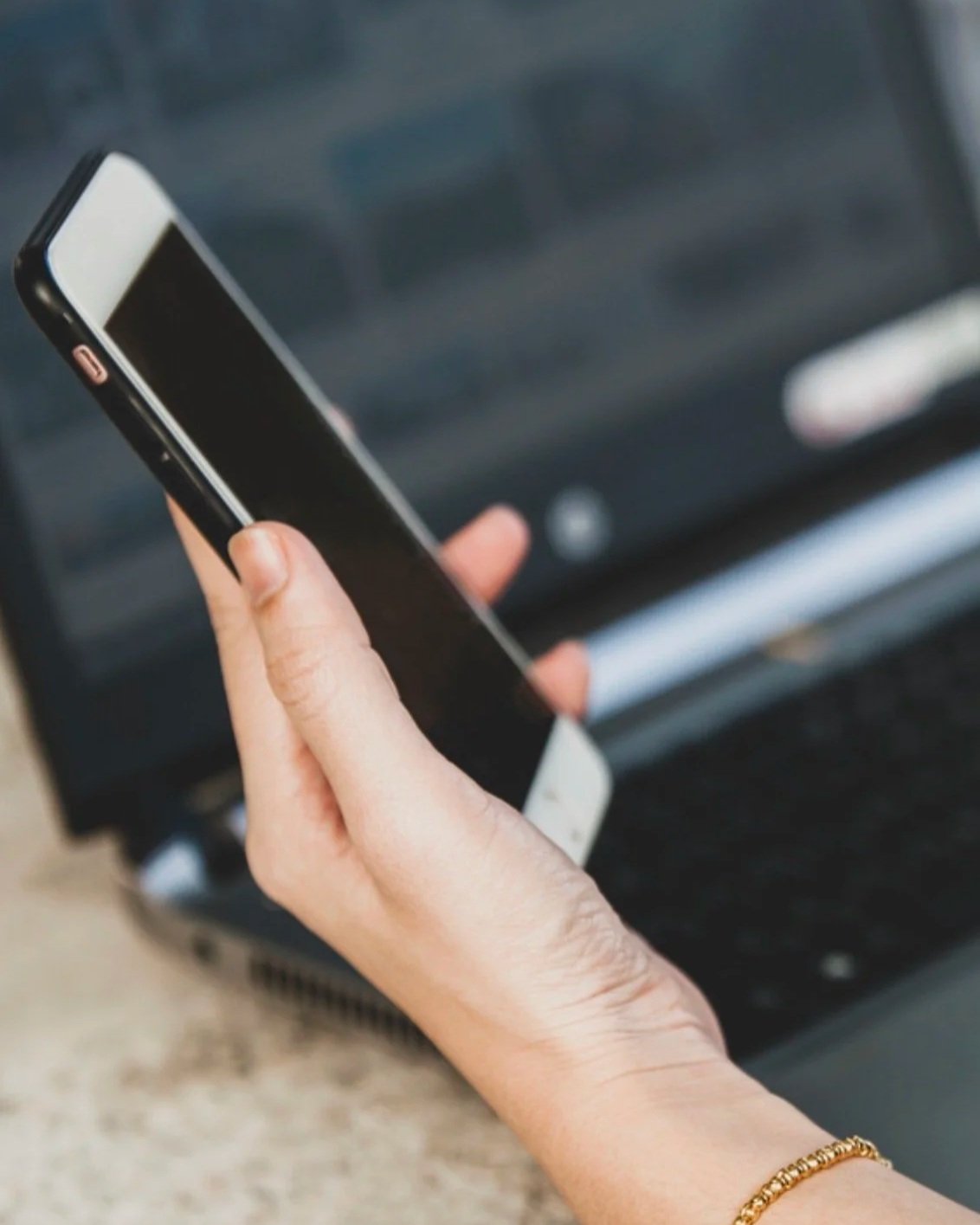 Close-up of a person holding a smartphone above a laptop keyboard, symbolizing personal branding, digital communication, and online decision-making.