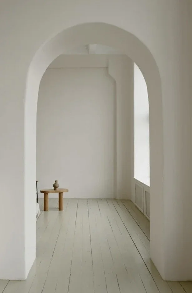 Minimal luxury interior with white walls, arched doorway, and natural light symbolizing white space and restraint in luxury real estate marketing.