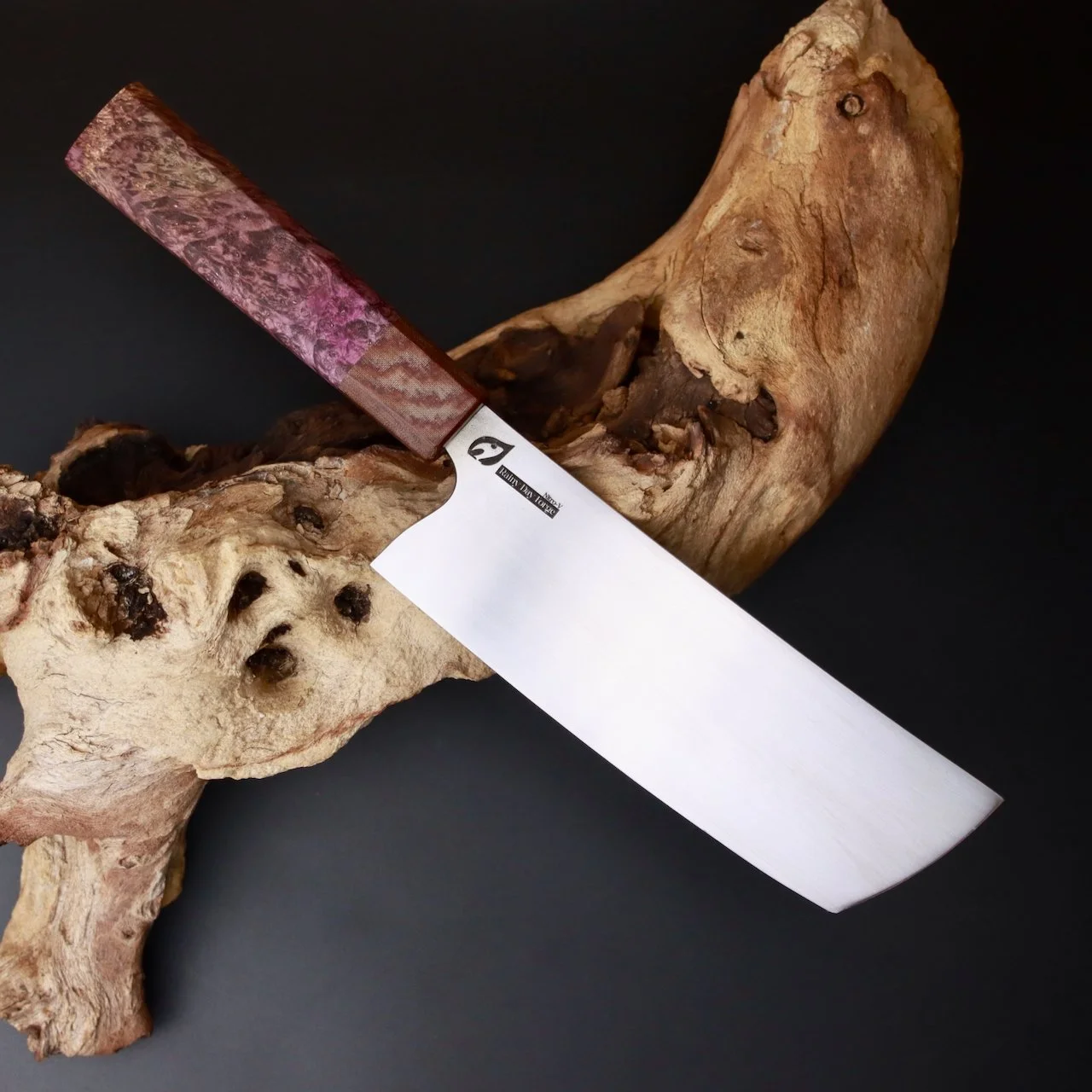A large calligraphy knife resting on a piece of knotted and textured driftwood with a dark background.