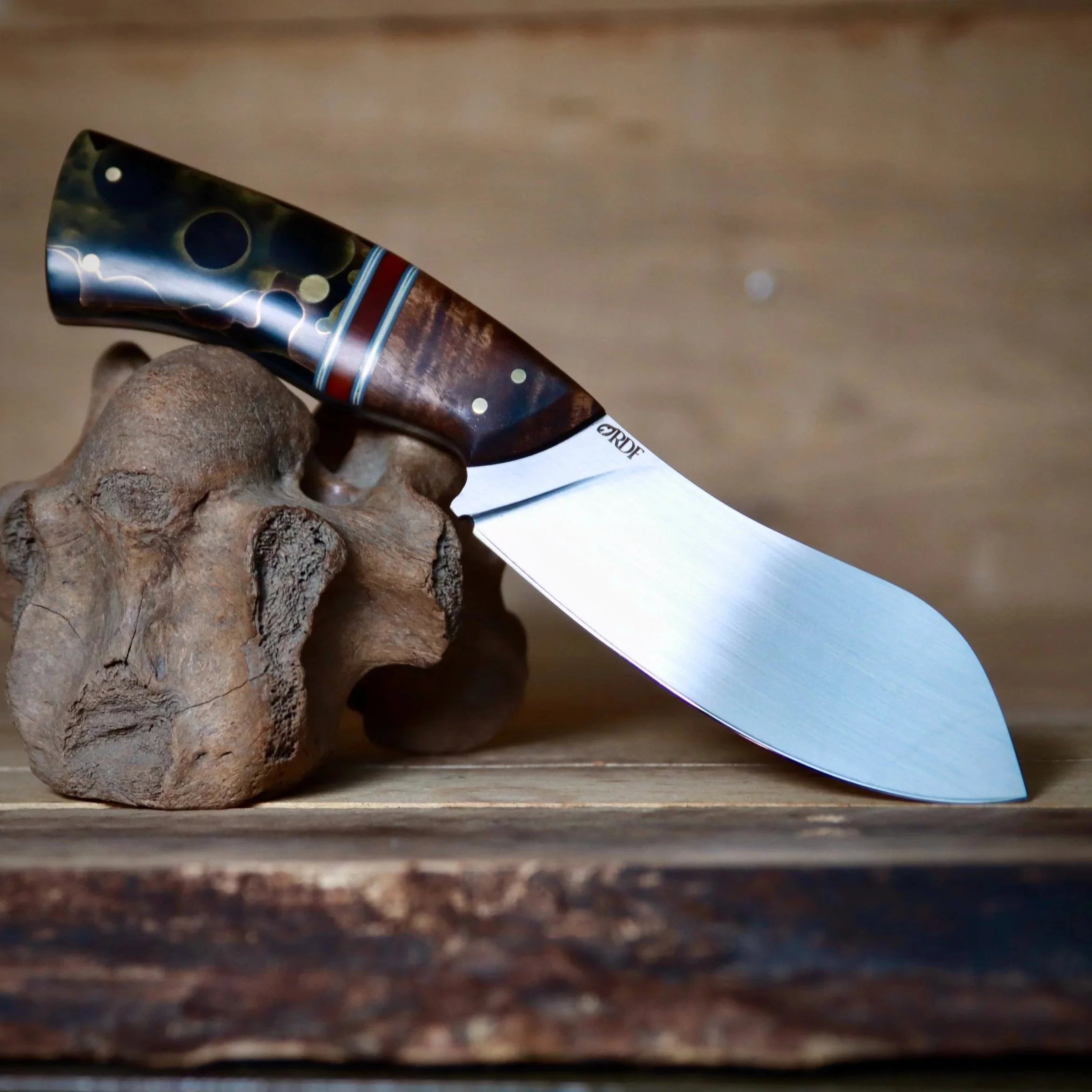 Close-up of a handmade or custom knife with a decorative handle resting on a textured wooden surface.