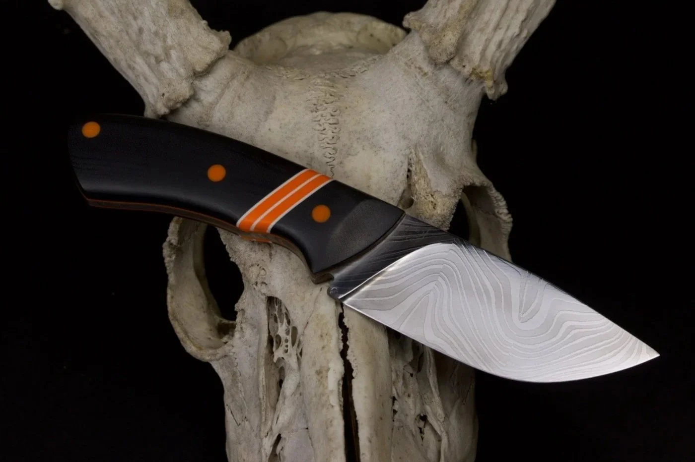 A folding pocket knife with a multi-colored handle and a patterned blade resting on a skull.
