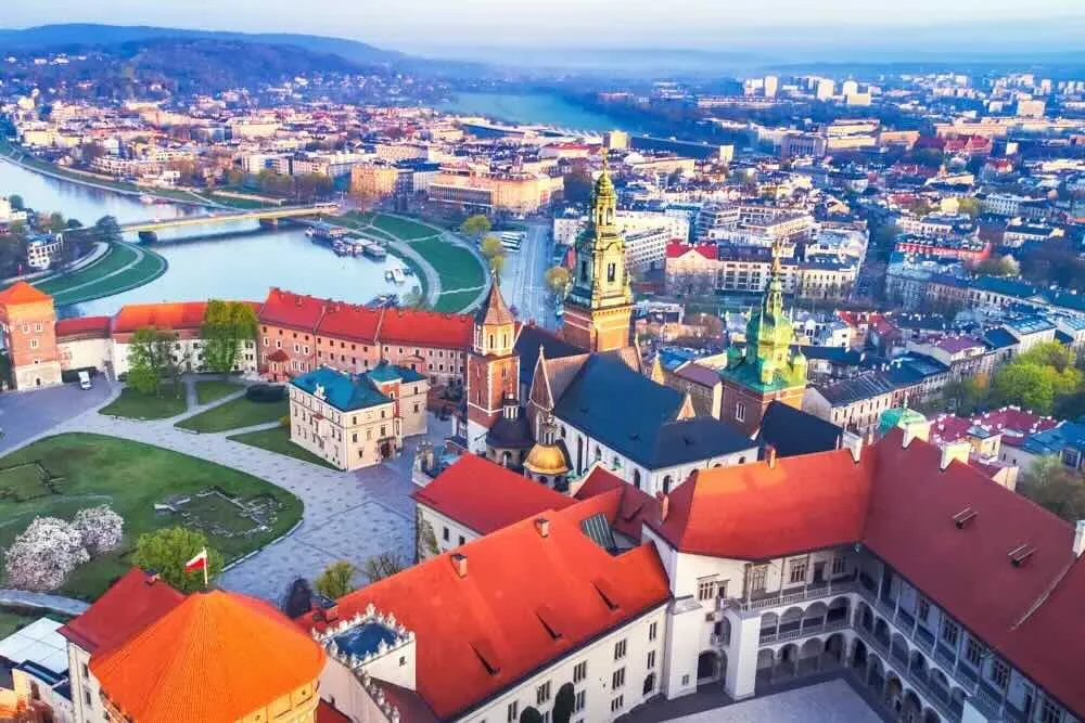 Aerial view of a historic European city with a river, bridges, and a castle with red roofs and spires.