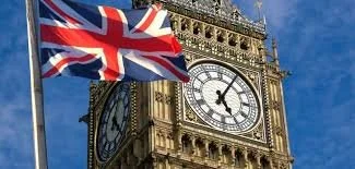 The iconic Big Ben clock tower with a Union Jack flag flying nearby against a blue sky.
