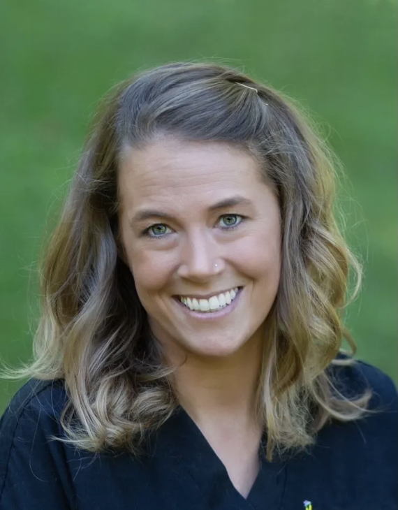 Smiling woman with wavy, shoulder-length hair outdoors on a green background.