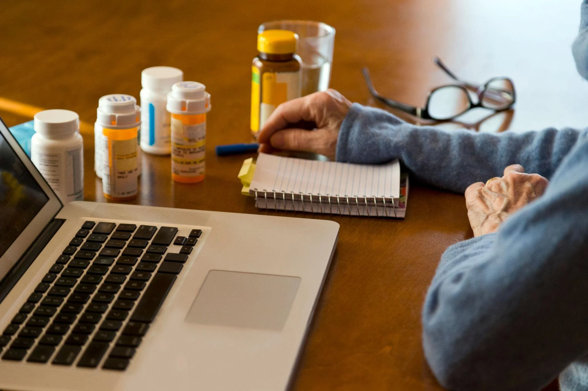persons arm, computer, notebook, and multiple bottles of medications
