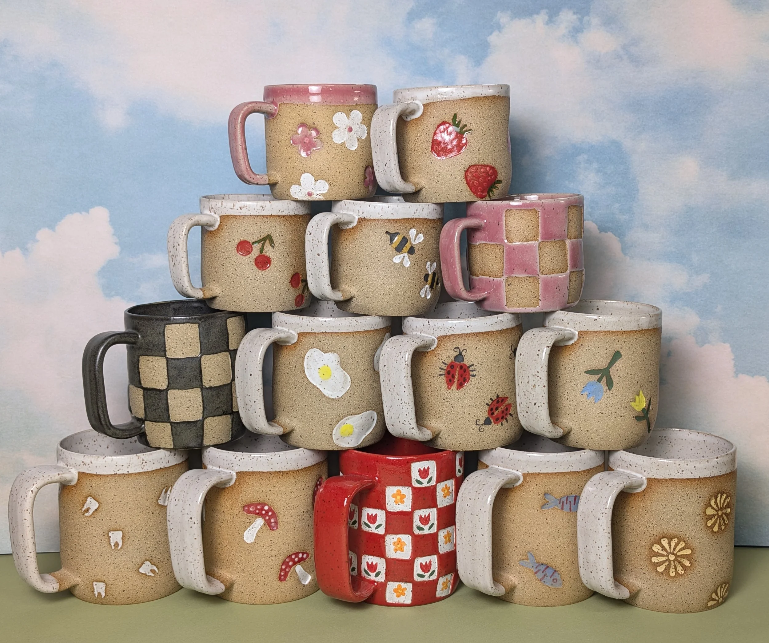 Stacked ceramic mugs with various decorative patterns, including olives, flowers, cherries, and checkerboard, against a light purple background.