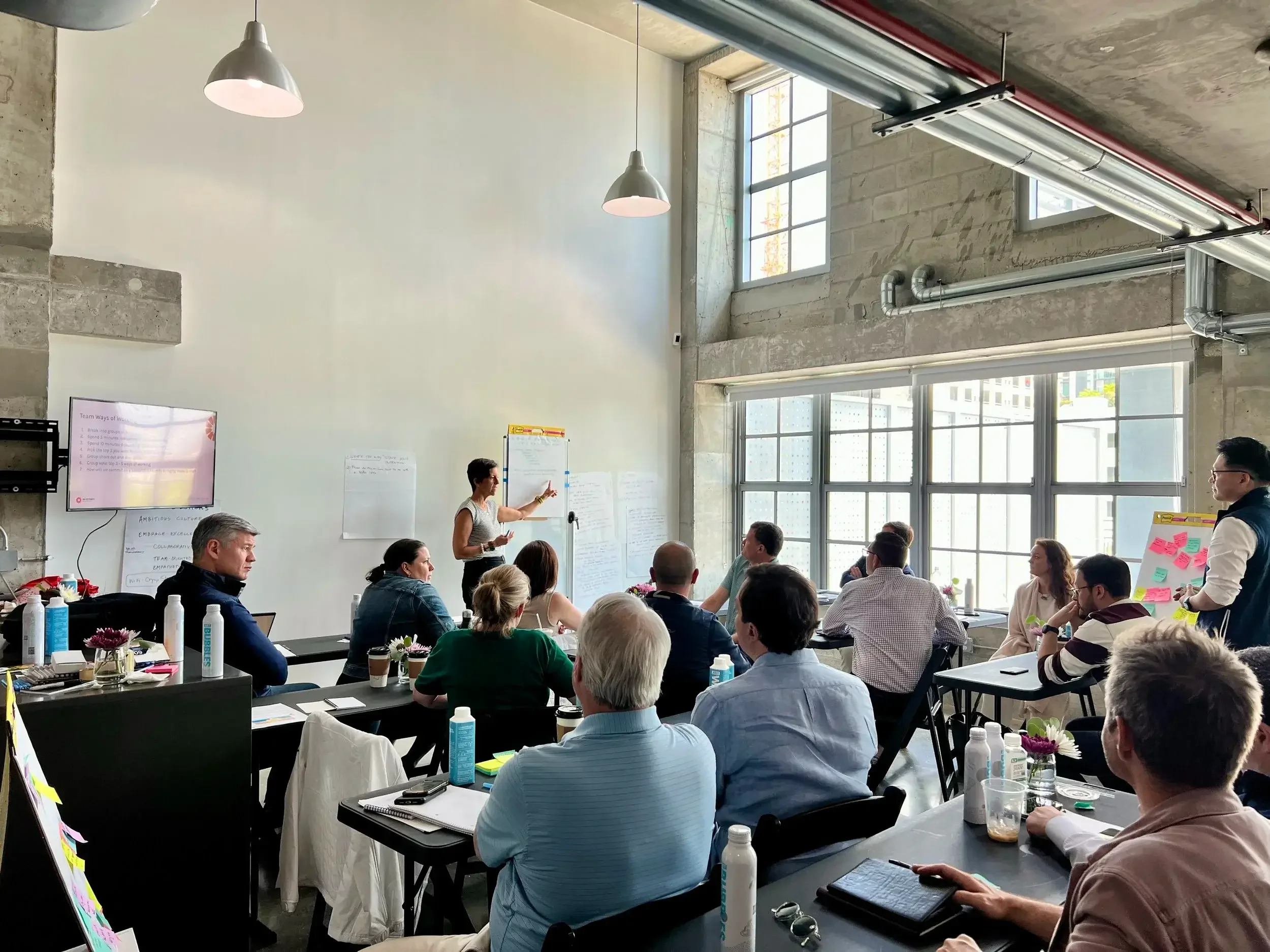 A group of people attending a Lead with Gina presentation in a bright, industrial-style conference room with large windows.
