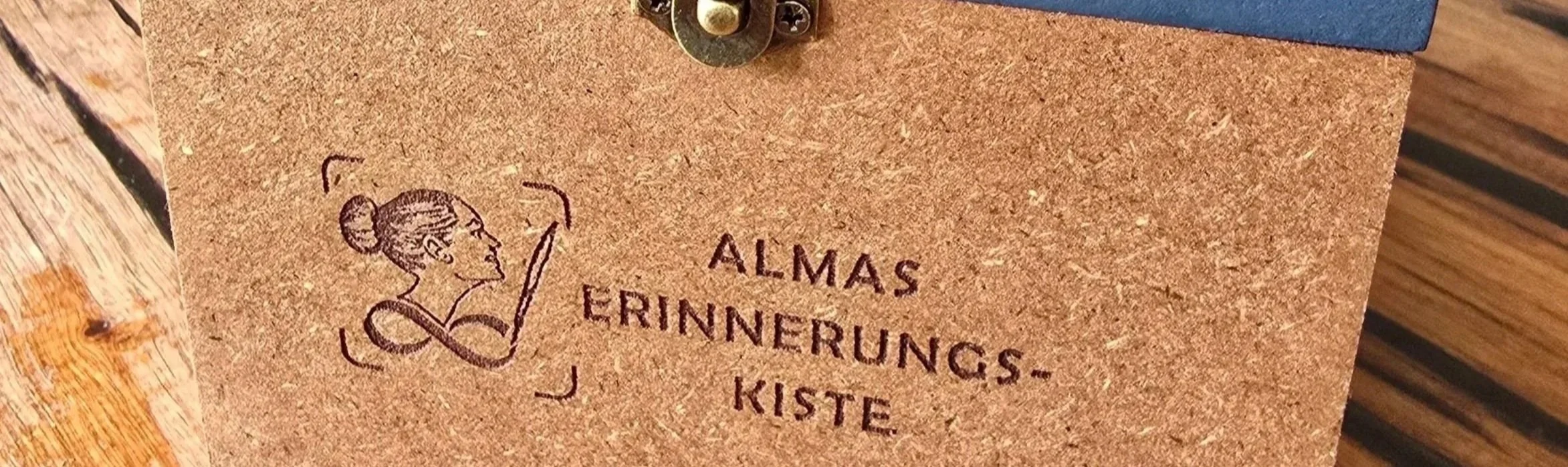 Das Bild zeigt die Gravur einer Erinnerungskiste für eine Person namens Alma. Die Gravur ist in die Frontseite der Erinnerungskiste in das MDF-Holz gelasert und hebt sich dunkel von dem Holz ab.