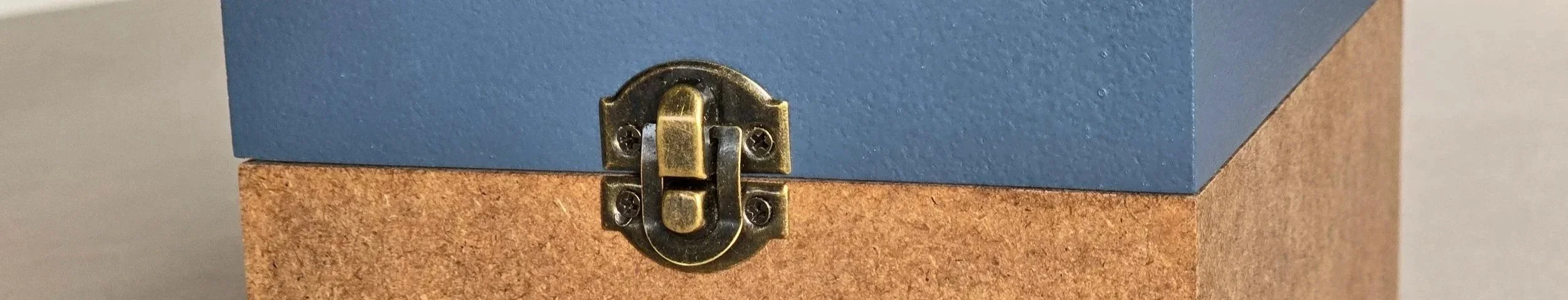 Nahaufnahme eines geschnitzten Holzkastens mit blauem Deckel und einer goldfarbenen Metallschließe.