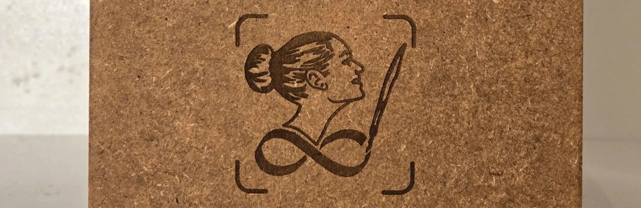 Eine stilisierte Illustration einer Frau mit einem hohen Dutt, die mit einem Bleistift schreibt, eingerahmt in einen Würfel auf braunem Hintergrund.