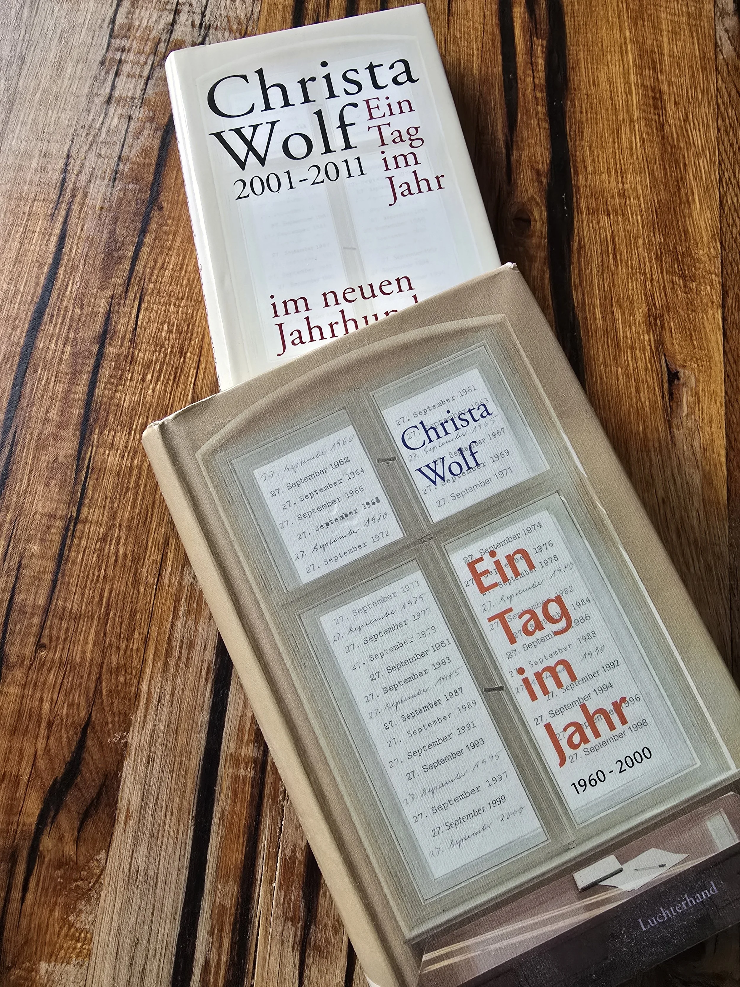 Zwei Bücher von Christa Wolf mit dem Titel 'Ein Tag im Jahr 2001-2011' und eines mit dem Titel '27. September 1964', liegen auf einem Holztisch.