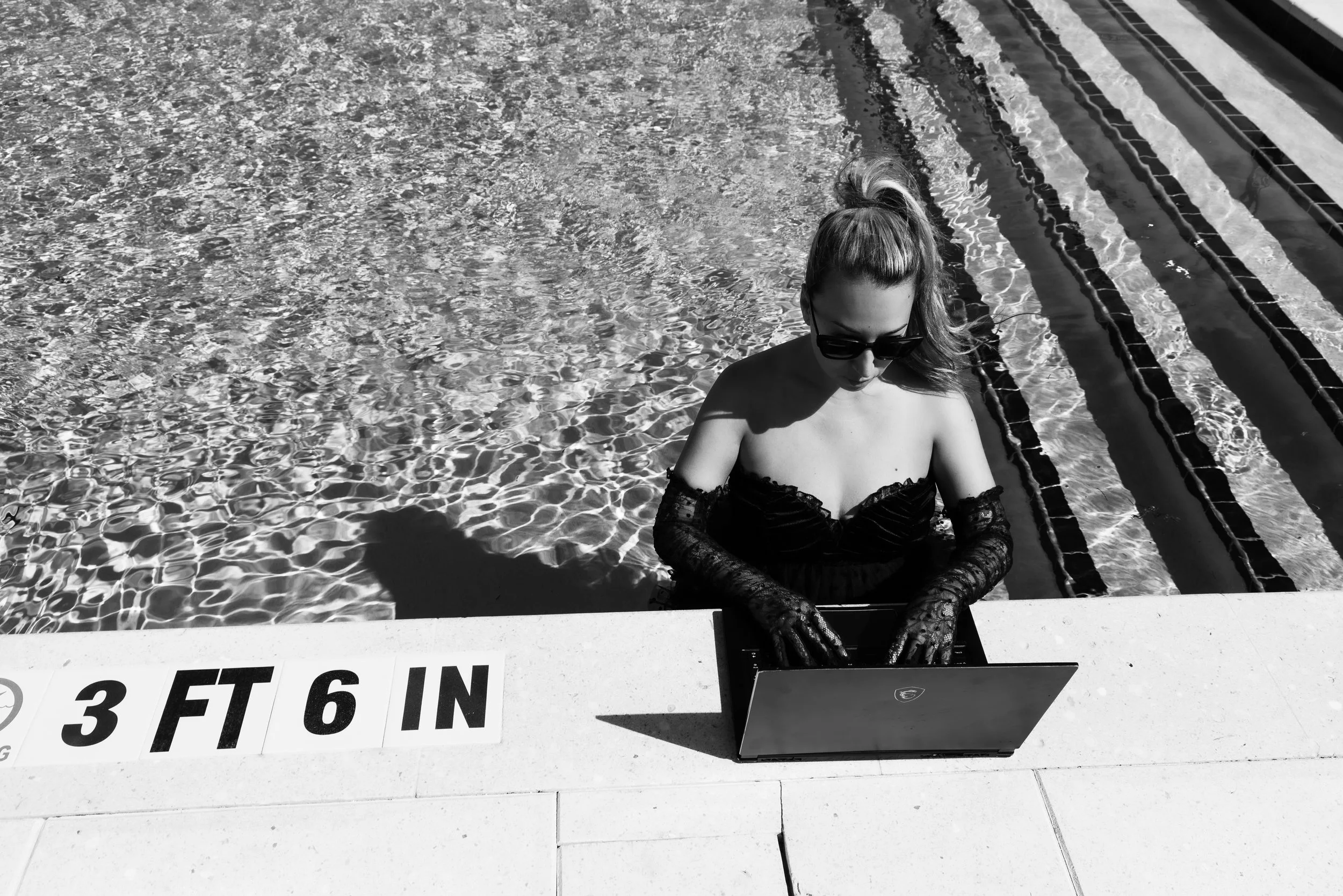a female digital marketer writing content on her laptop on the edge of a pool while standing in a pool on