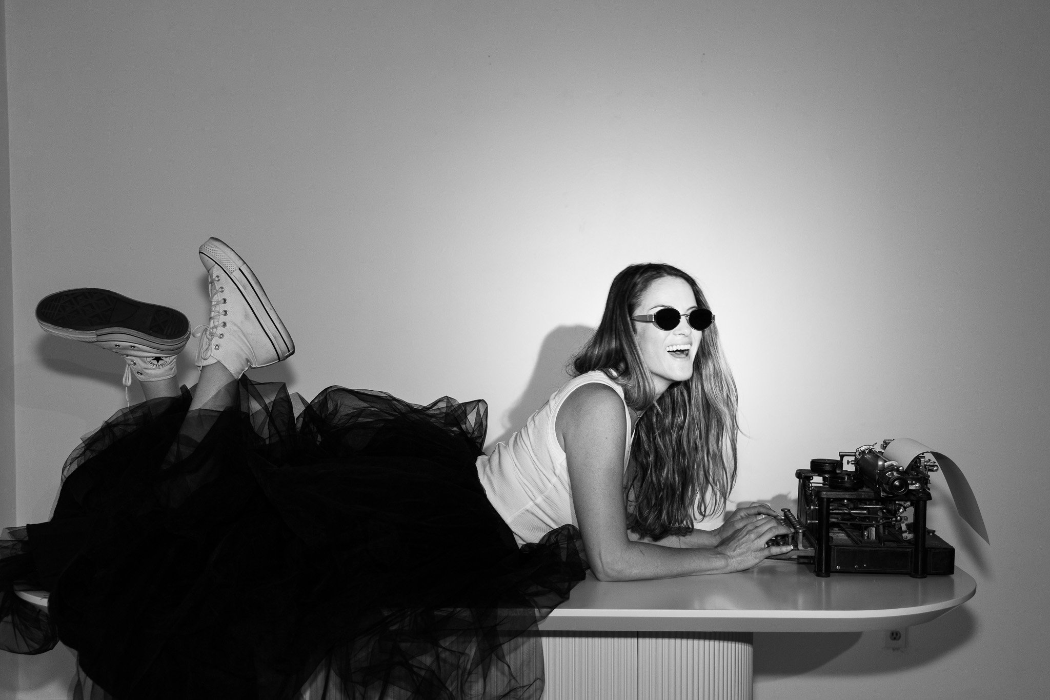 A woman in a dress and sunglasses lays on a table while she types on a typewriter about how blogs help SEO rankings