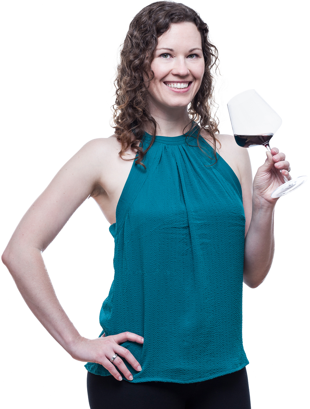 A woman with curly brown hair smiling and holding a glass of red wine, wearing a sleeveless teal top.