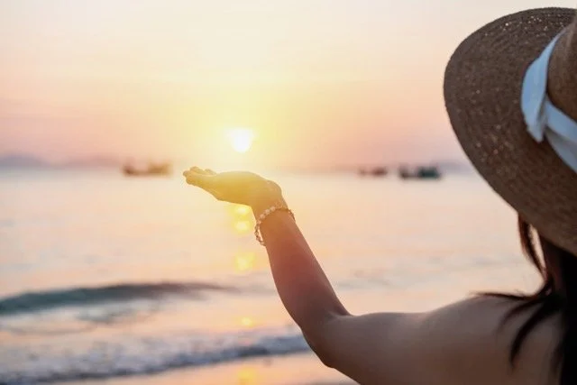 Woman standing in ocean waves at sunrise with outstretched hand
