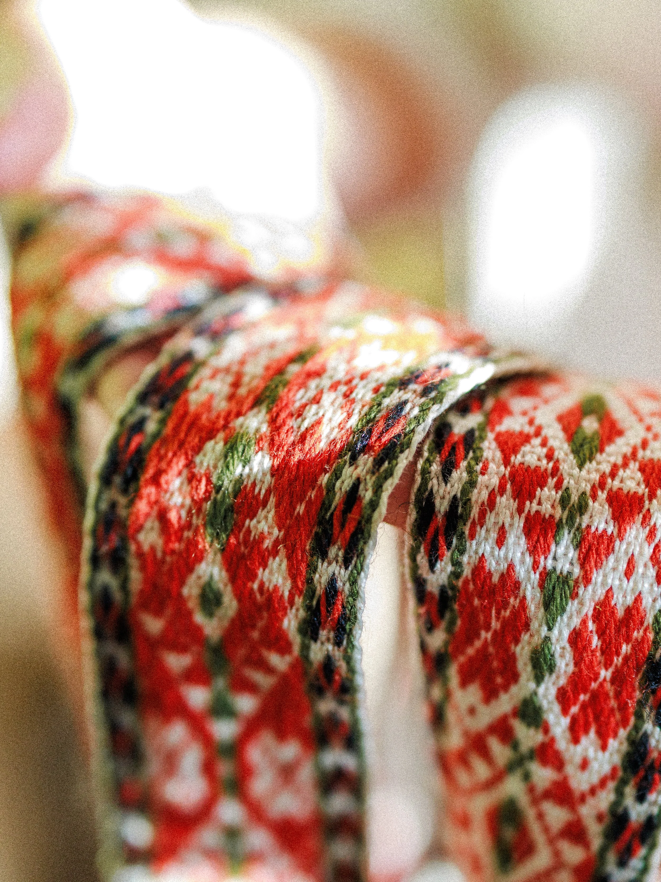 Close-up of a decorated woven fabric with red, white, green, and black patterns, draped over an object with blurred background.