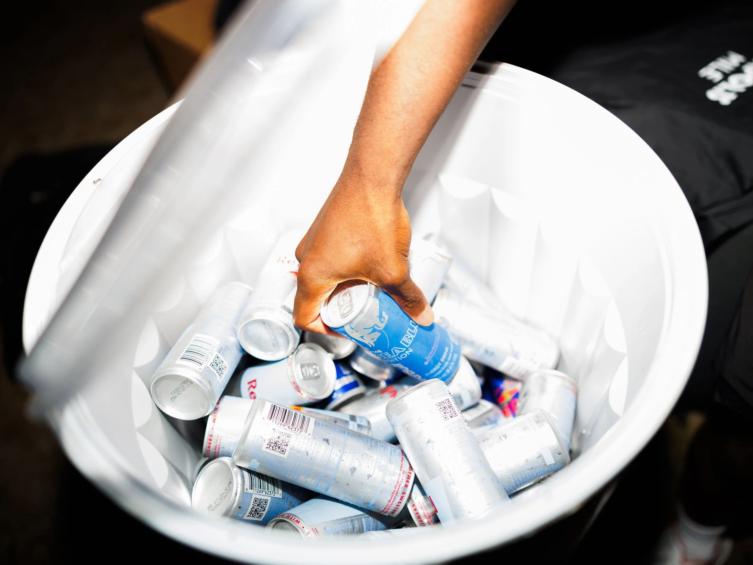A hand reaching into a white cooler filled with Red Bull cans.