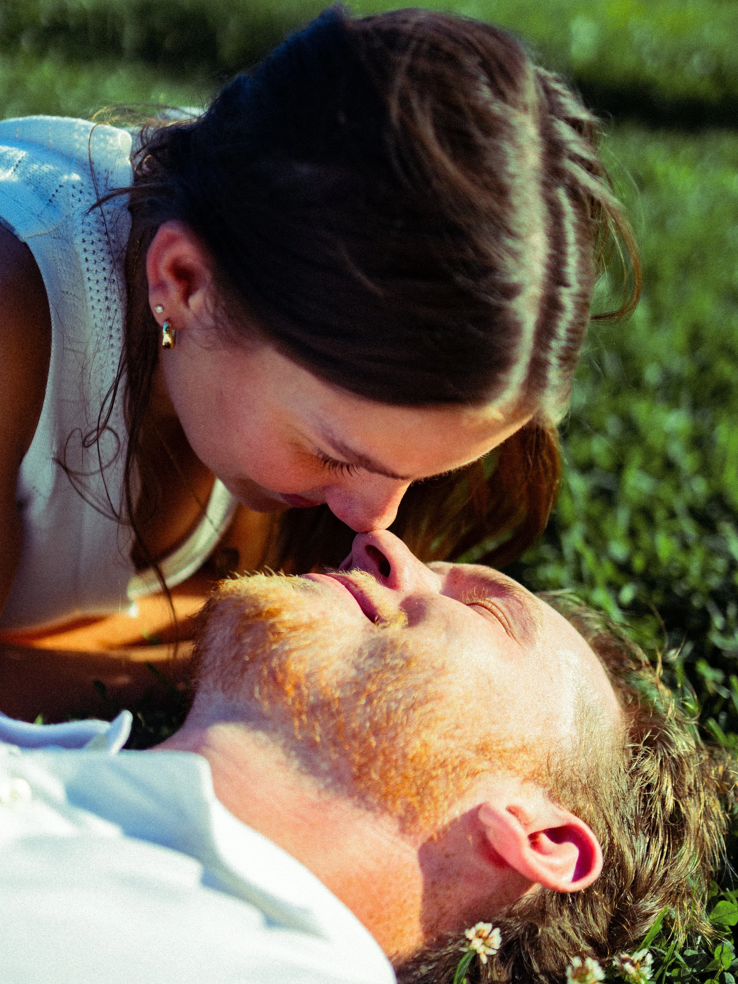 A woman is leaning over a man lying on the grass, about to kiss him.