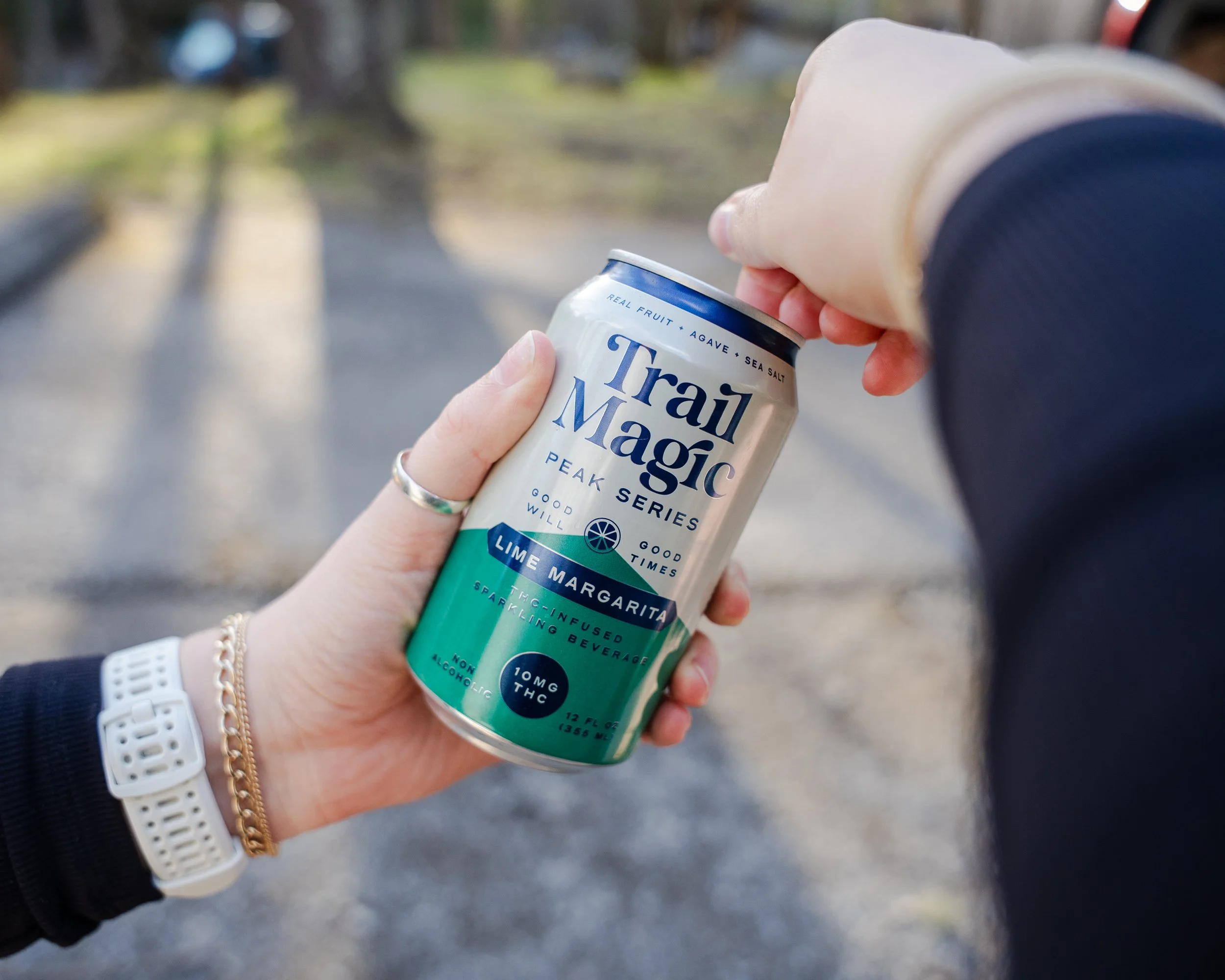 Person holding a can of Trail Magic Lime Margarita sparkling beverage with a hand and a blurred outdoor background.