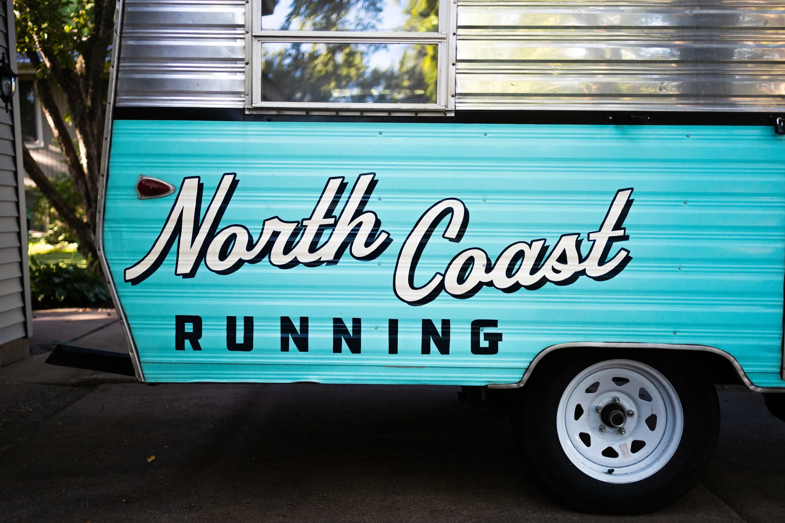 A teal-colored trailer with the words 'North Coast Running' painted on the side.