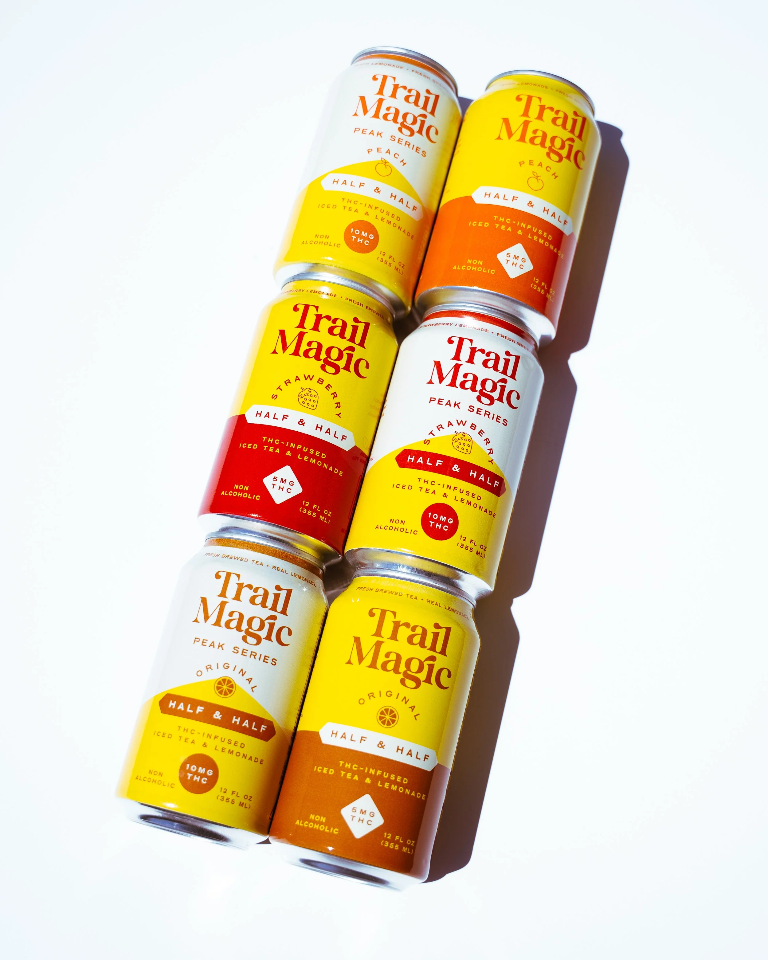 Six cans of Trai Magic THC-infused iced tea and lemonade in various flavors, arranged in a pattern on a white background.