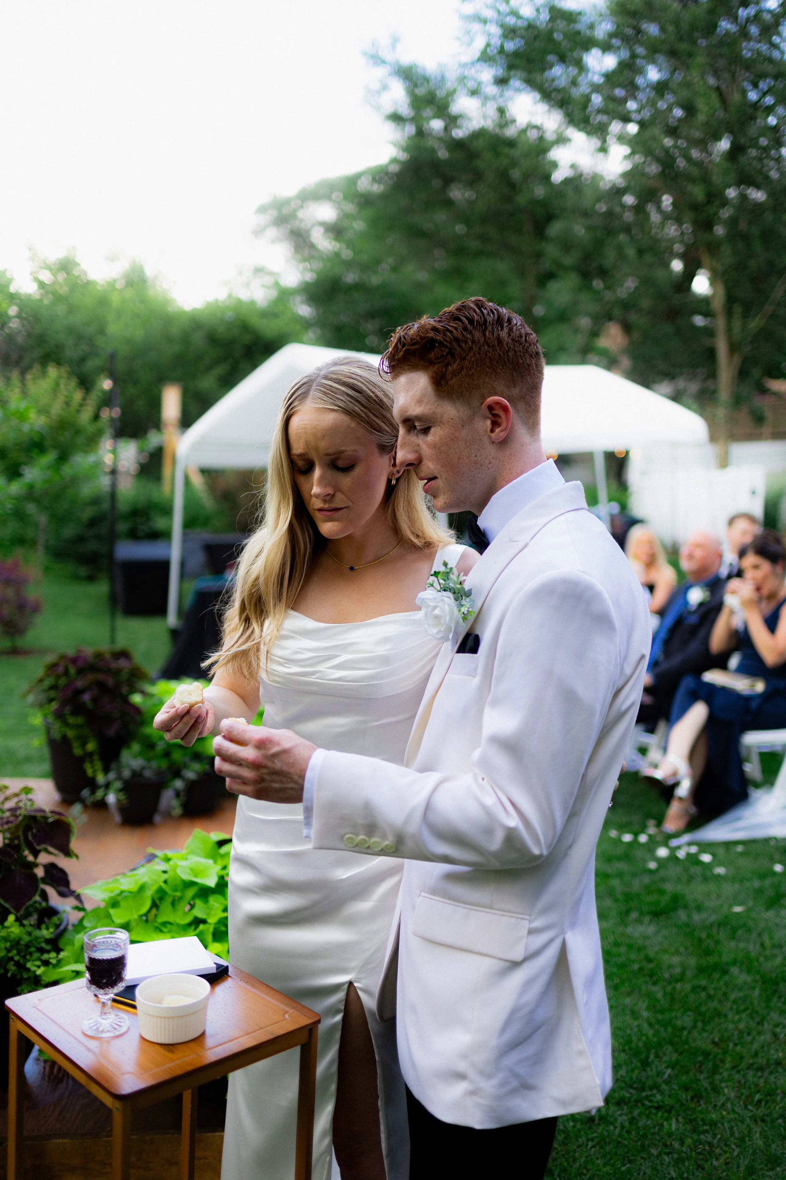 Bride and groom exchanging vows during outdoor wedding ceremony with seated guests in background.