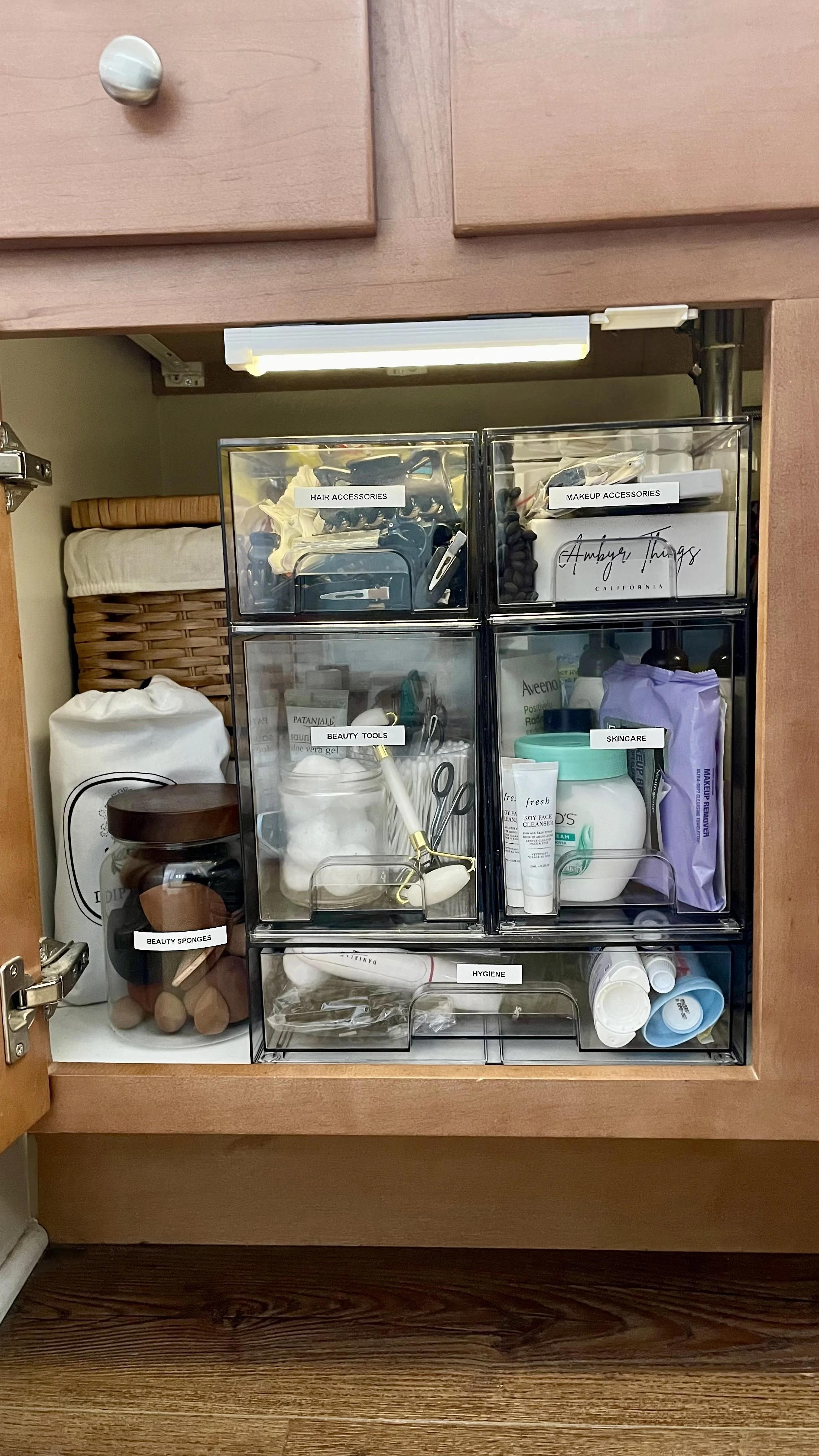 Under sink bathroom storage with labeled acrylic organizers for skincare, hair tools, and beauty products