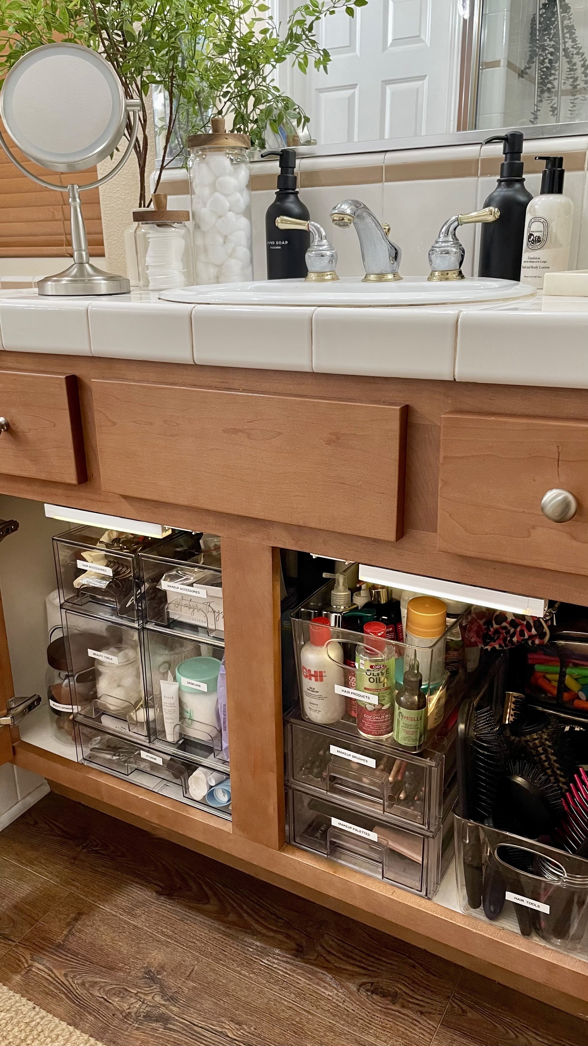 Organized bathroom vanity with labeled clear bins, under cabinet lighting, and clutter-free countertop