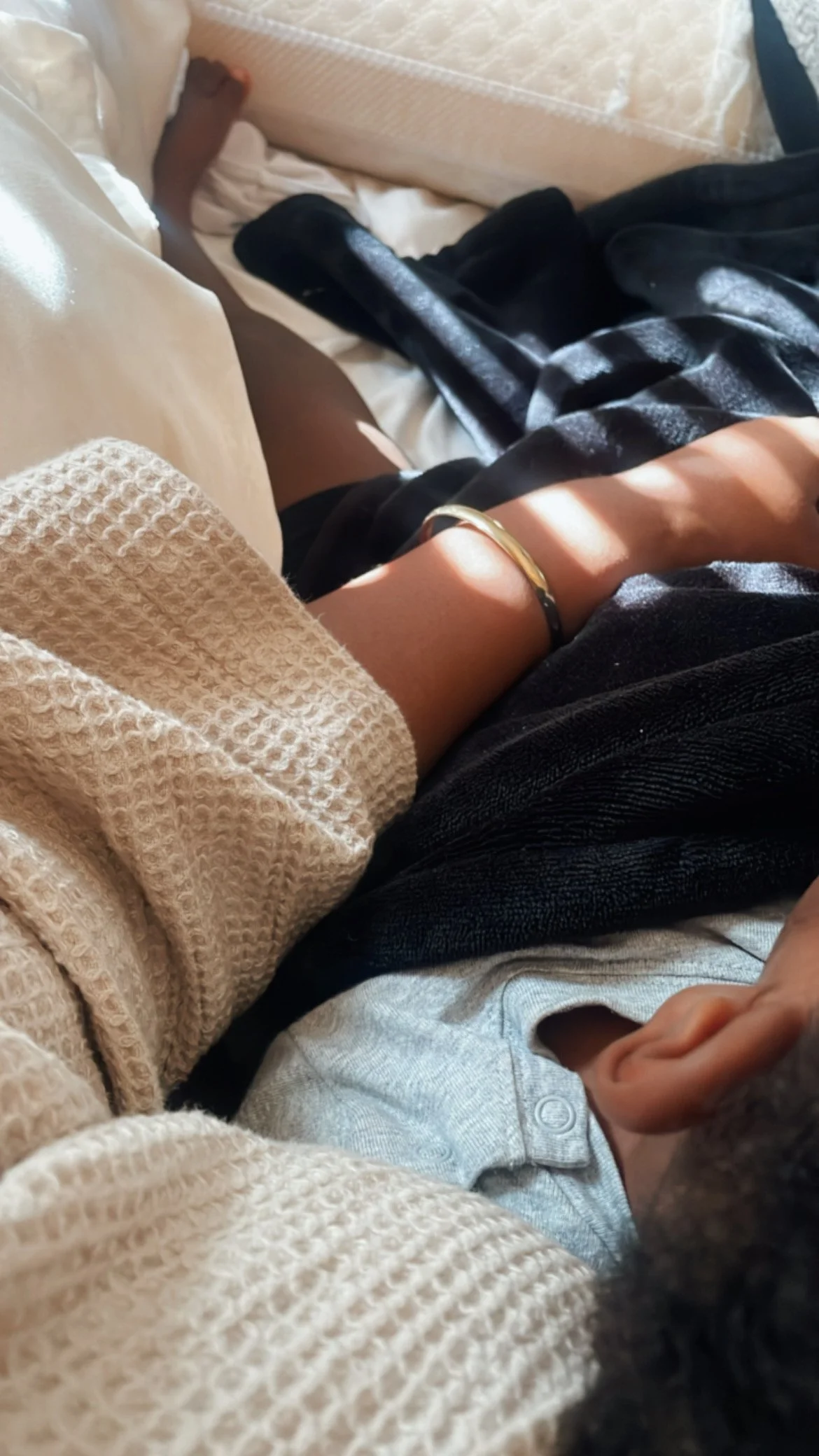 The arms of a woman wearing a gold bracelet snuggling a little boy in her arms