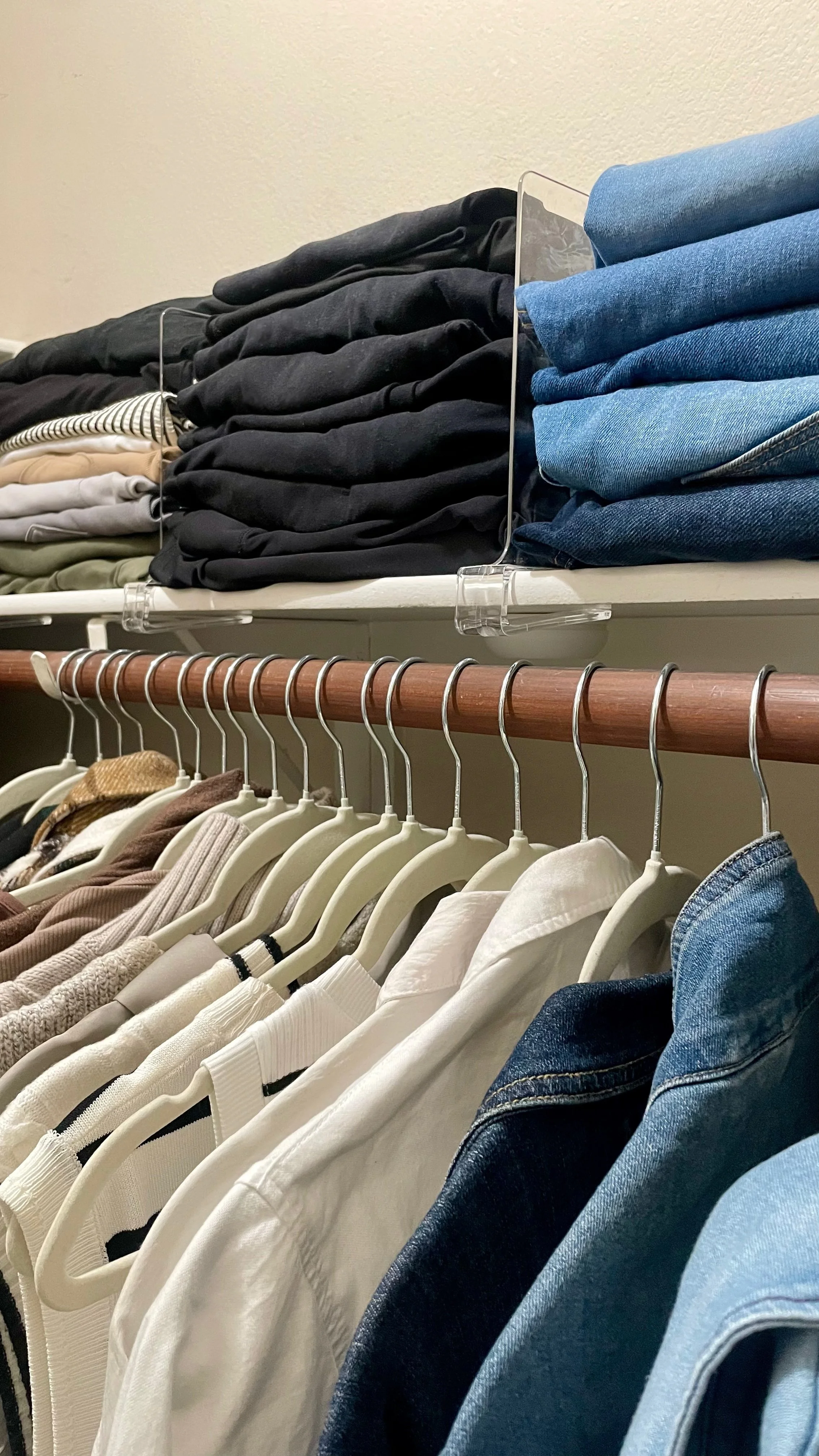 Neutral wardrobe on cream velvet hangers with folded denim and clear shelf dividers for closet organization