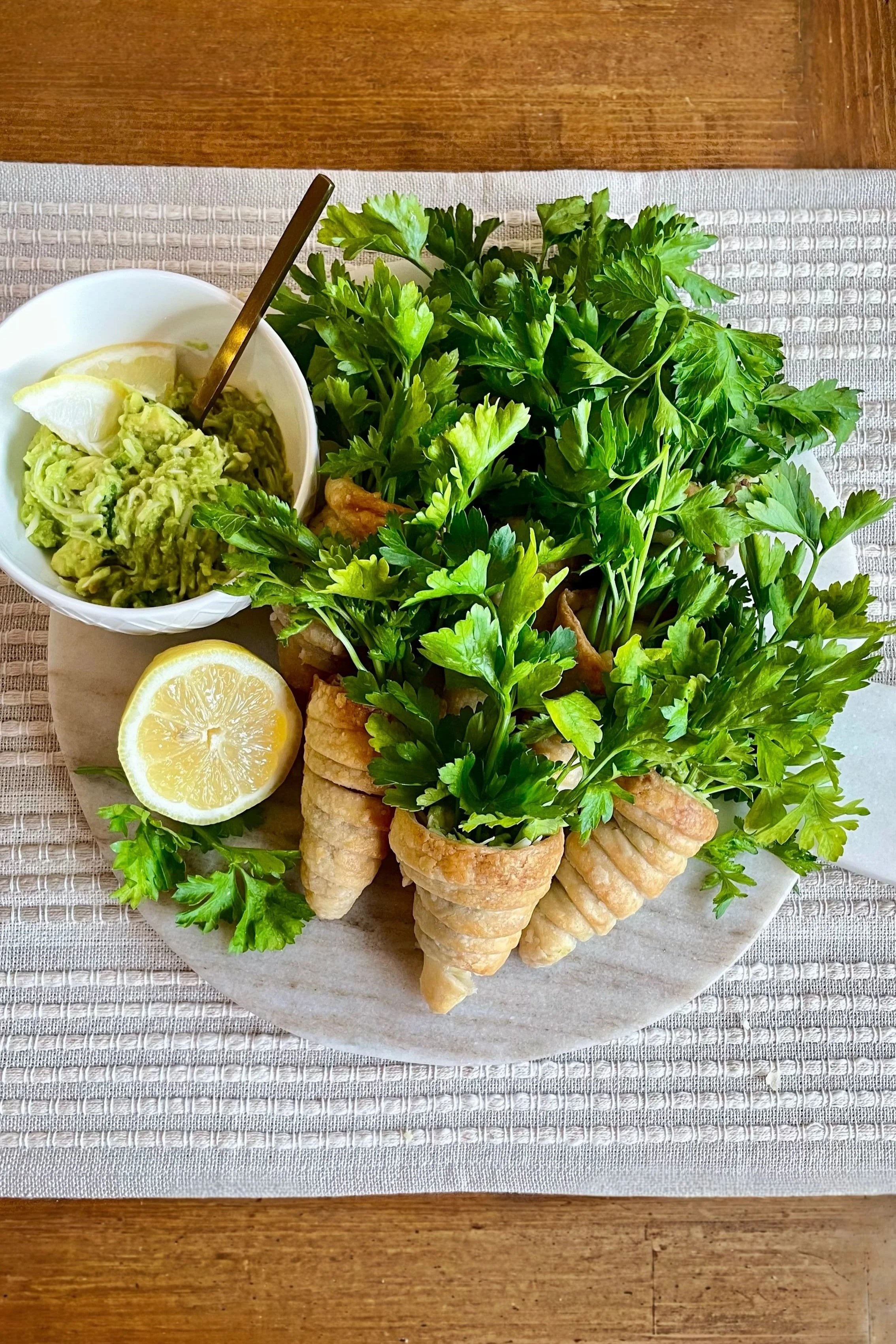 Golden puff pastry carrots arranged on a marble board with fresh parsley stems and a lemon half, styled on a neutral table setting