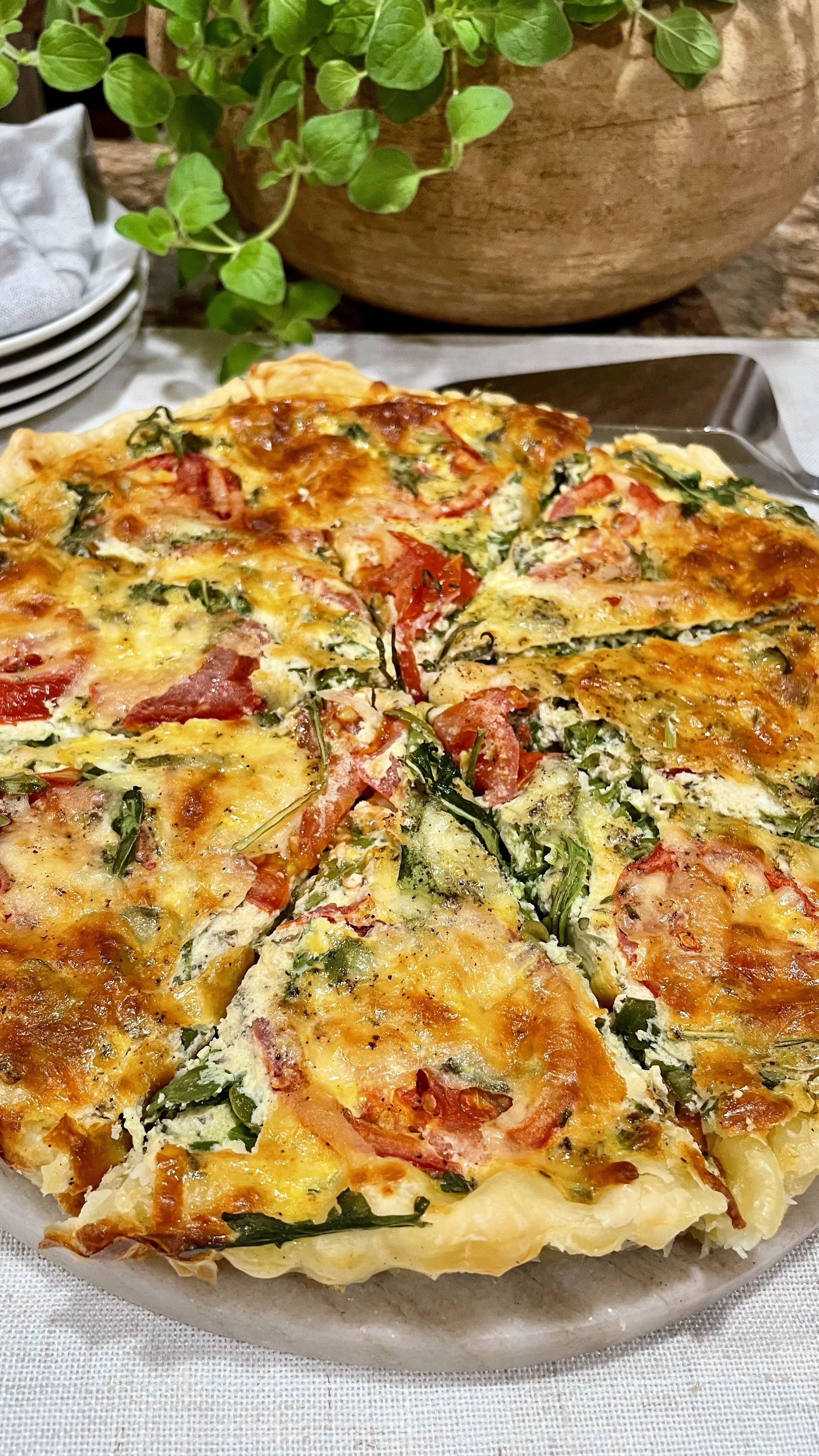 Close-up of baked herb quiche with golden crust, fresh herbs, tomatoes, and melted cheese