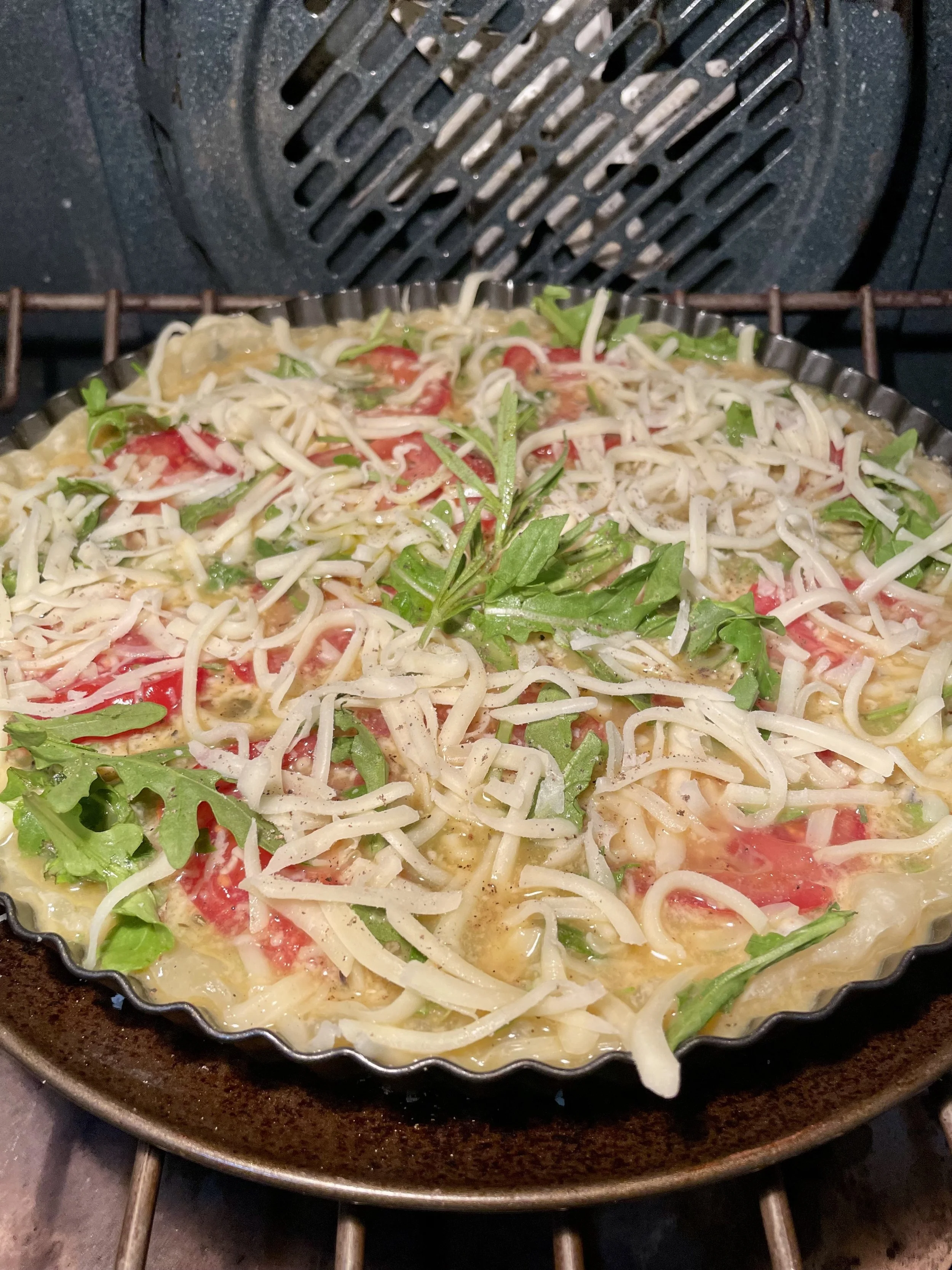 Unbaked herb quiche with eggs, tomatoes, arugula, and cheese being placed in the oven