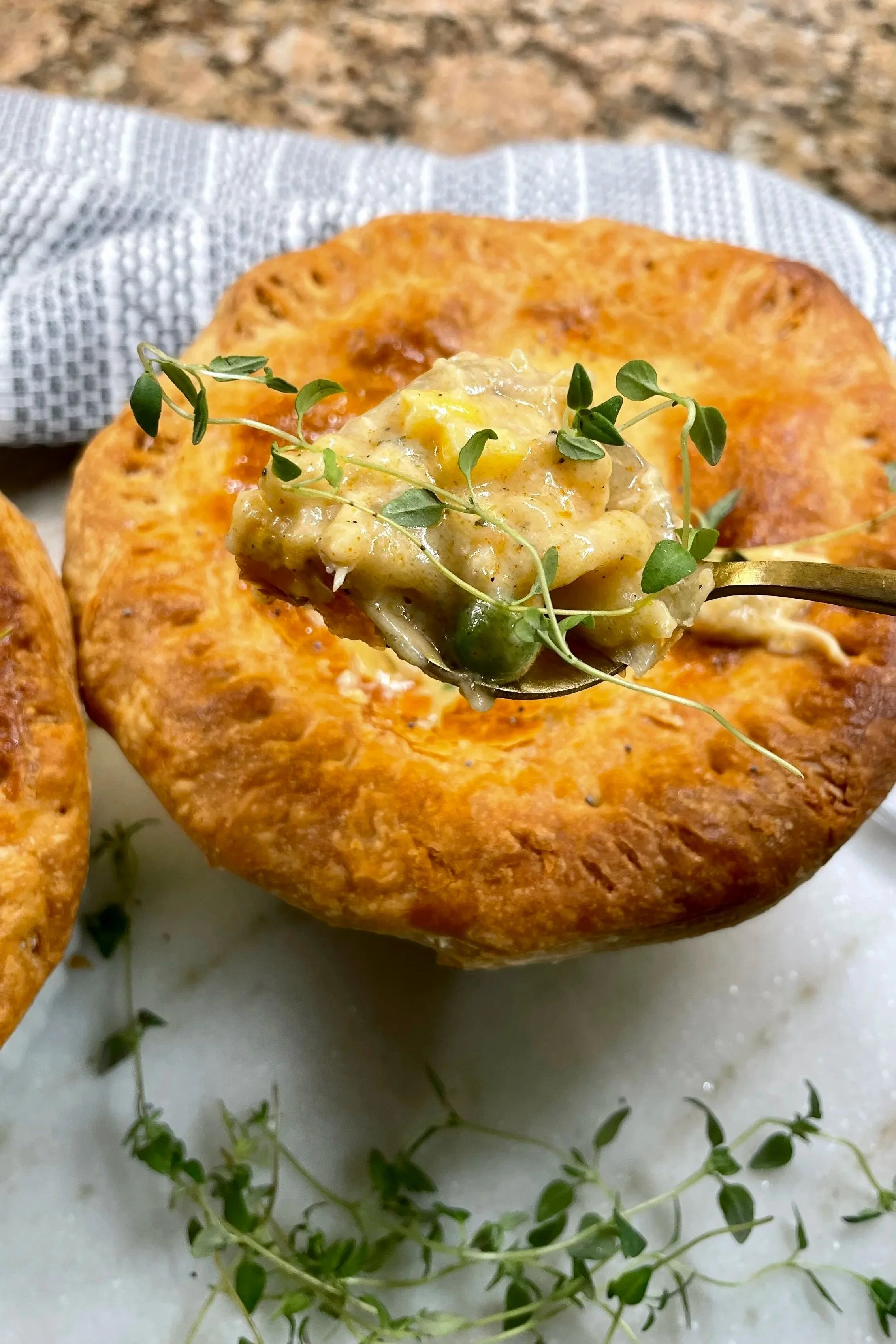 A spoonful of creamy chicken pot pie filling with tender chicken, vegetables, and fresh thyme held above a golden, flaky individual pot pie.