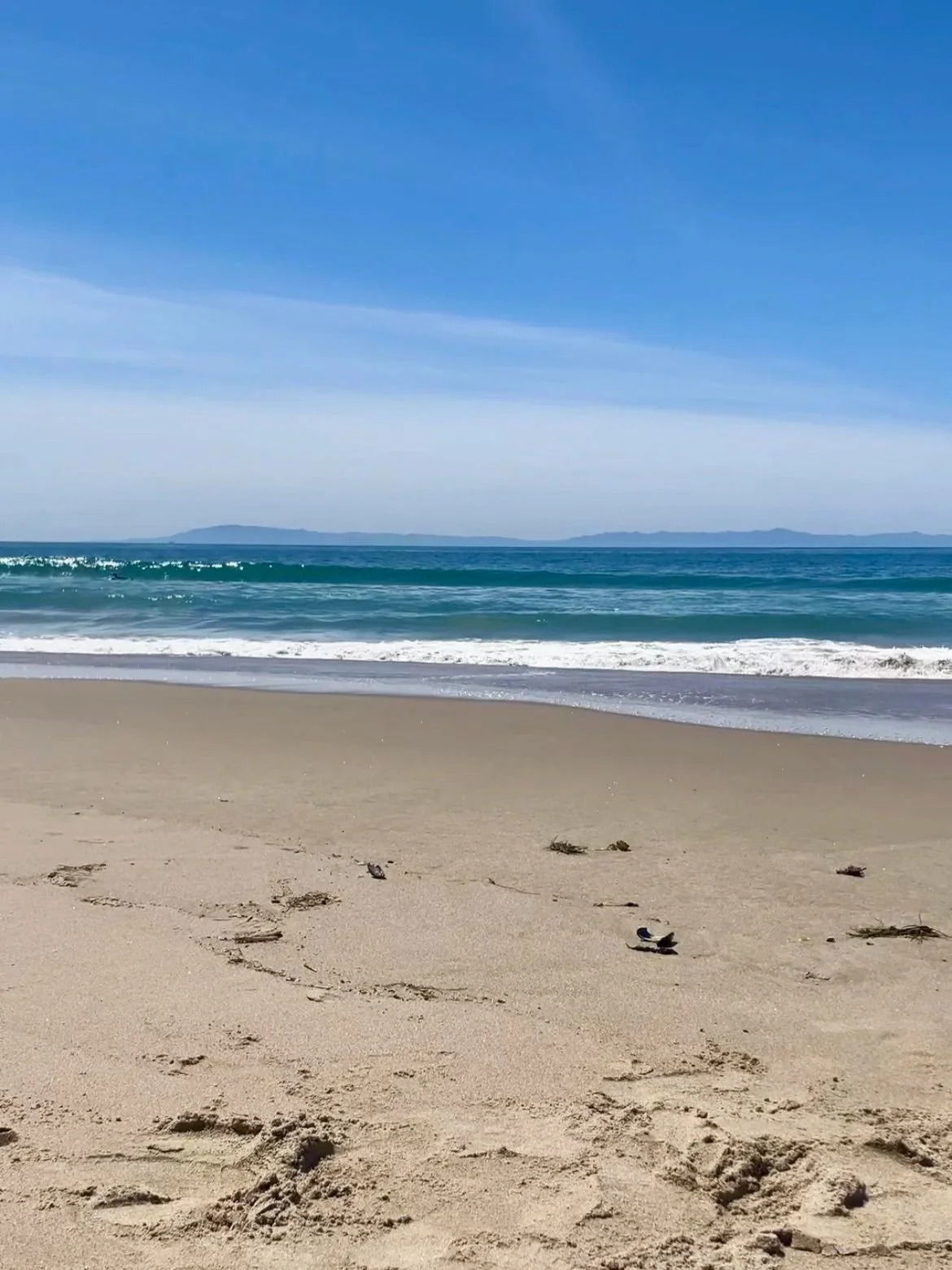 Ocean waves rolling onto a quiet Southern California beach beneath a bright blue sky, representing rest and slowing down.