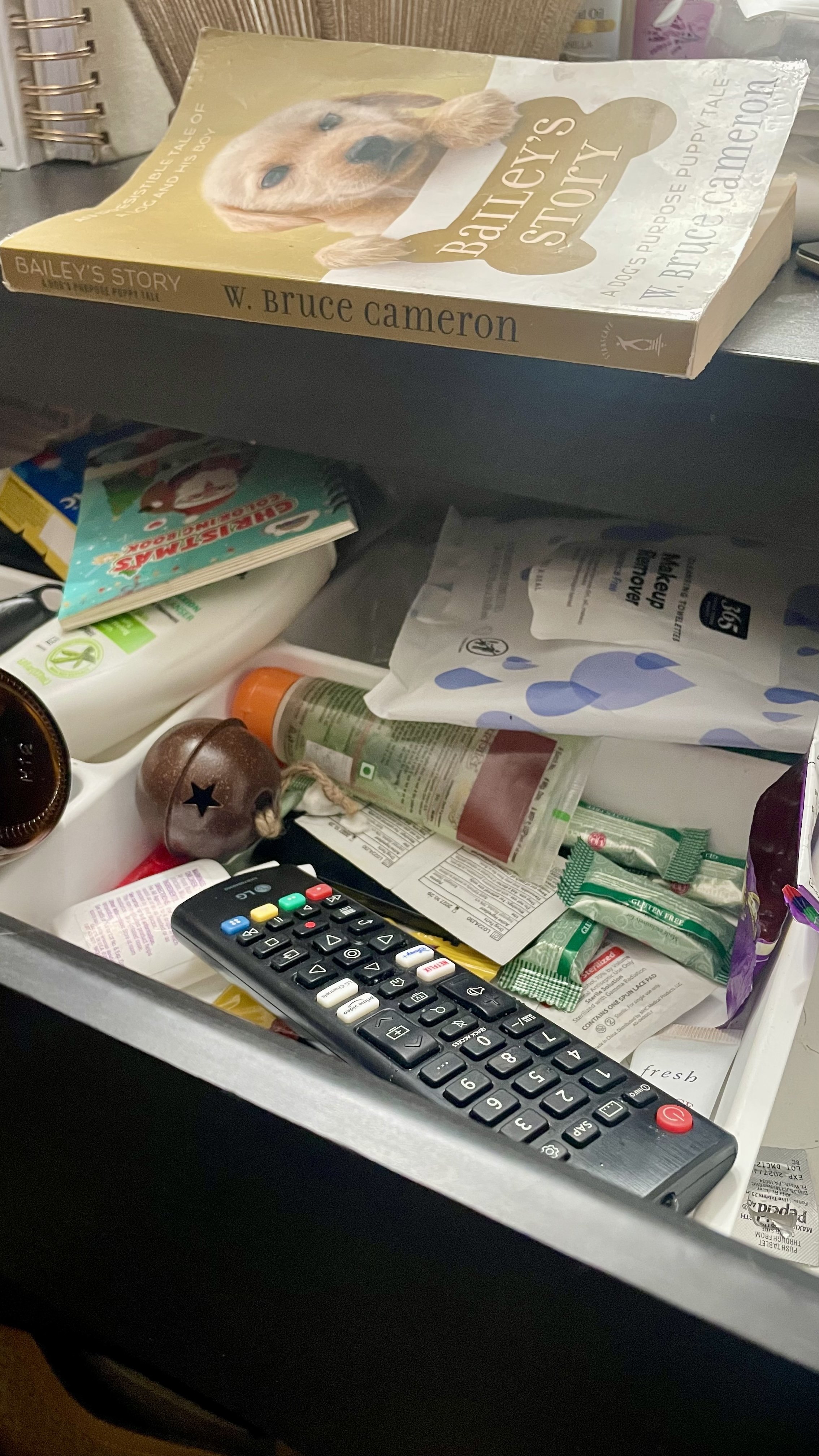 Overstuffed bedside drawer with random items including remote, wipes, book, and miscellaneous products creating visual and mental clutter.