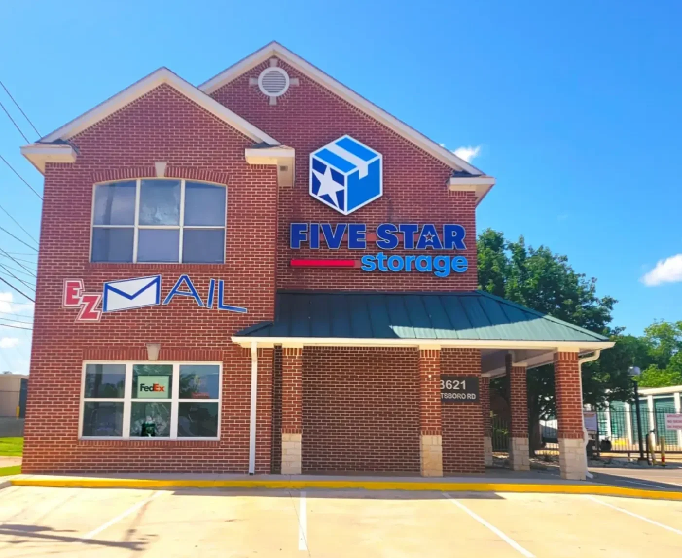 Red brick building with signs for Five Star Storage, Mail, and FedEx. Located at 3621 TSboro Rd, with a parking lot in front and trees in the background, under a blue sky with some clouds.