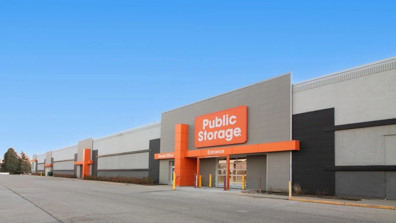 Exterior view of a Public Storage facility with a large orange sign and a mostly empty parking lot.