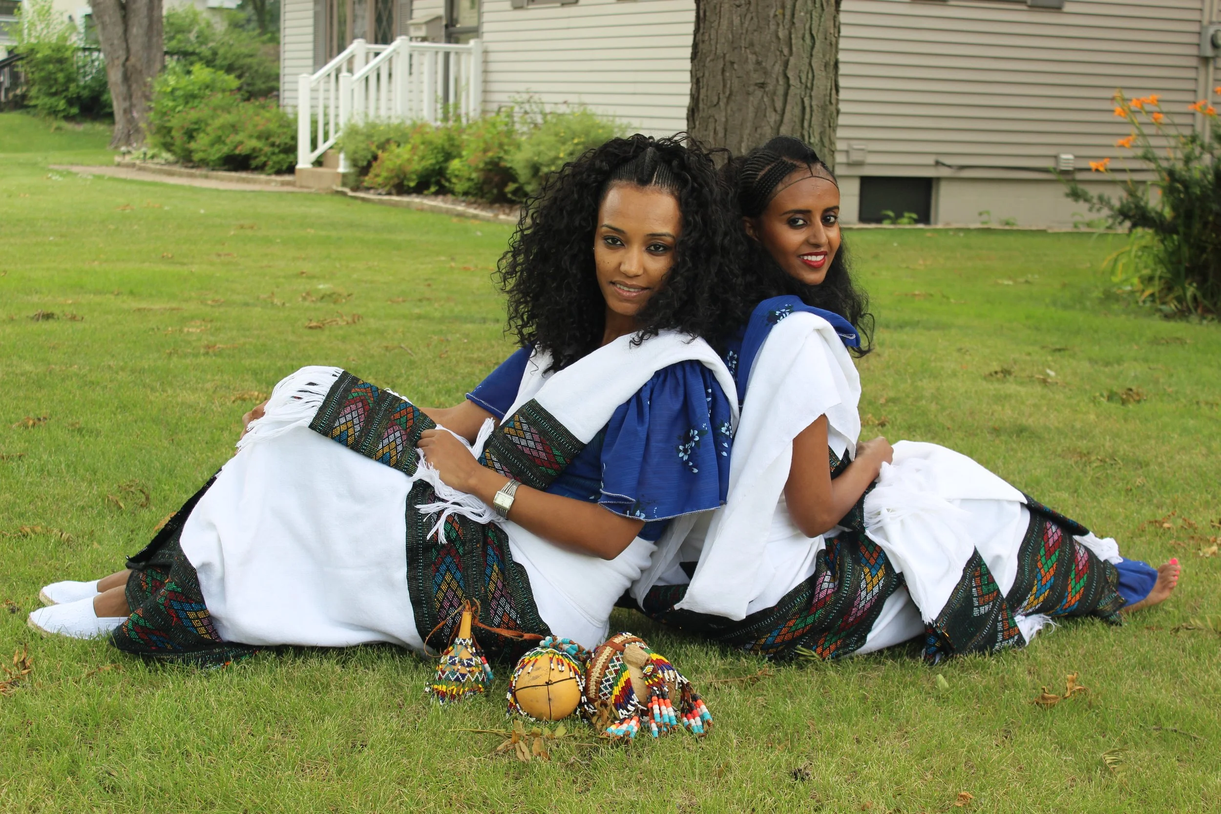 Two women wearing traditional Raya traditional clothing sitting on grass with their backs against each other in 2018, Santa Clara, CA.