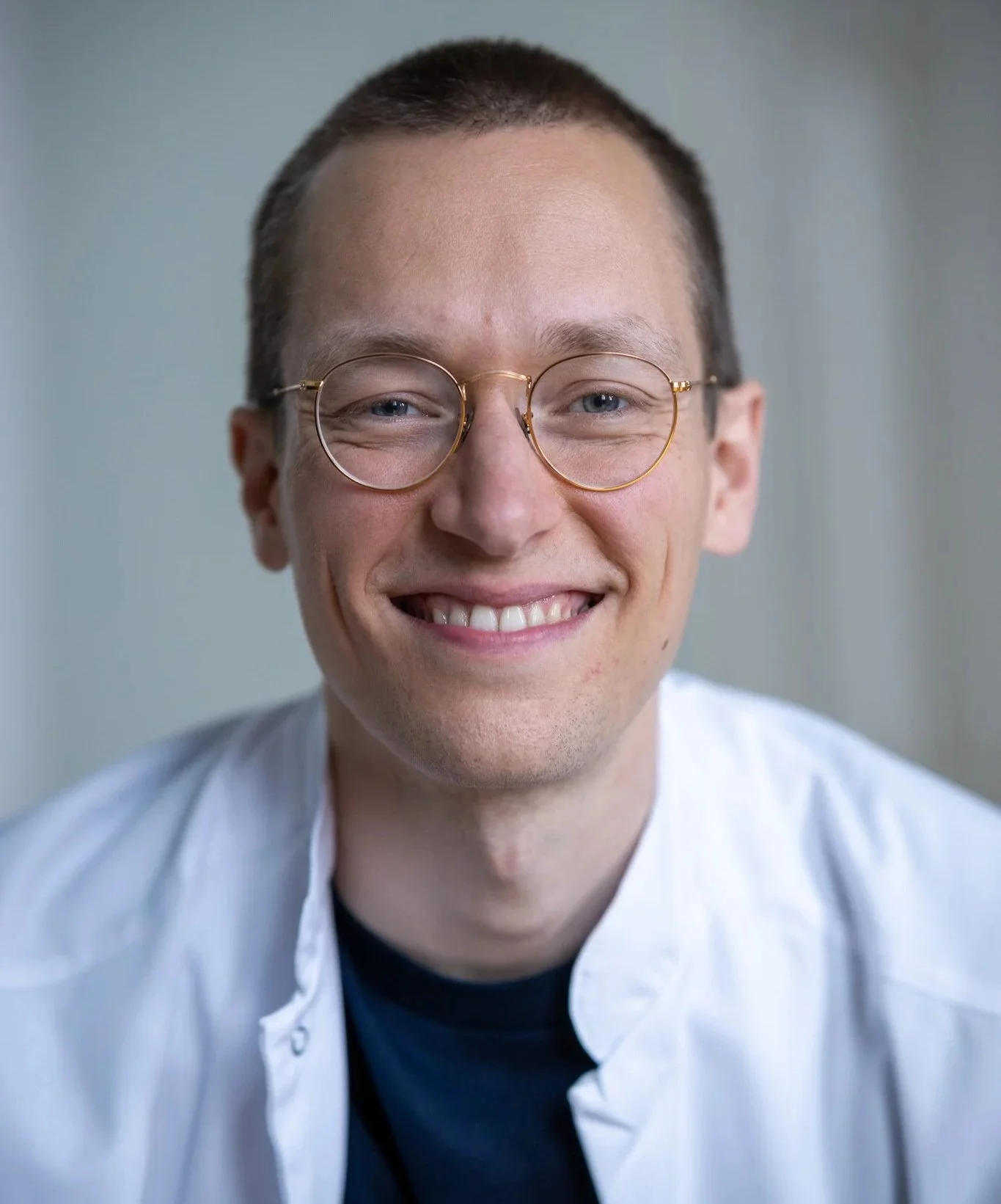 Lächelnder Mann mit Brille, dunklem T-Shirt und weißer Jacke, Nahaufnahme